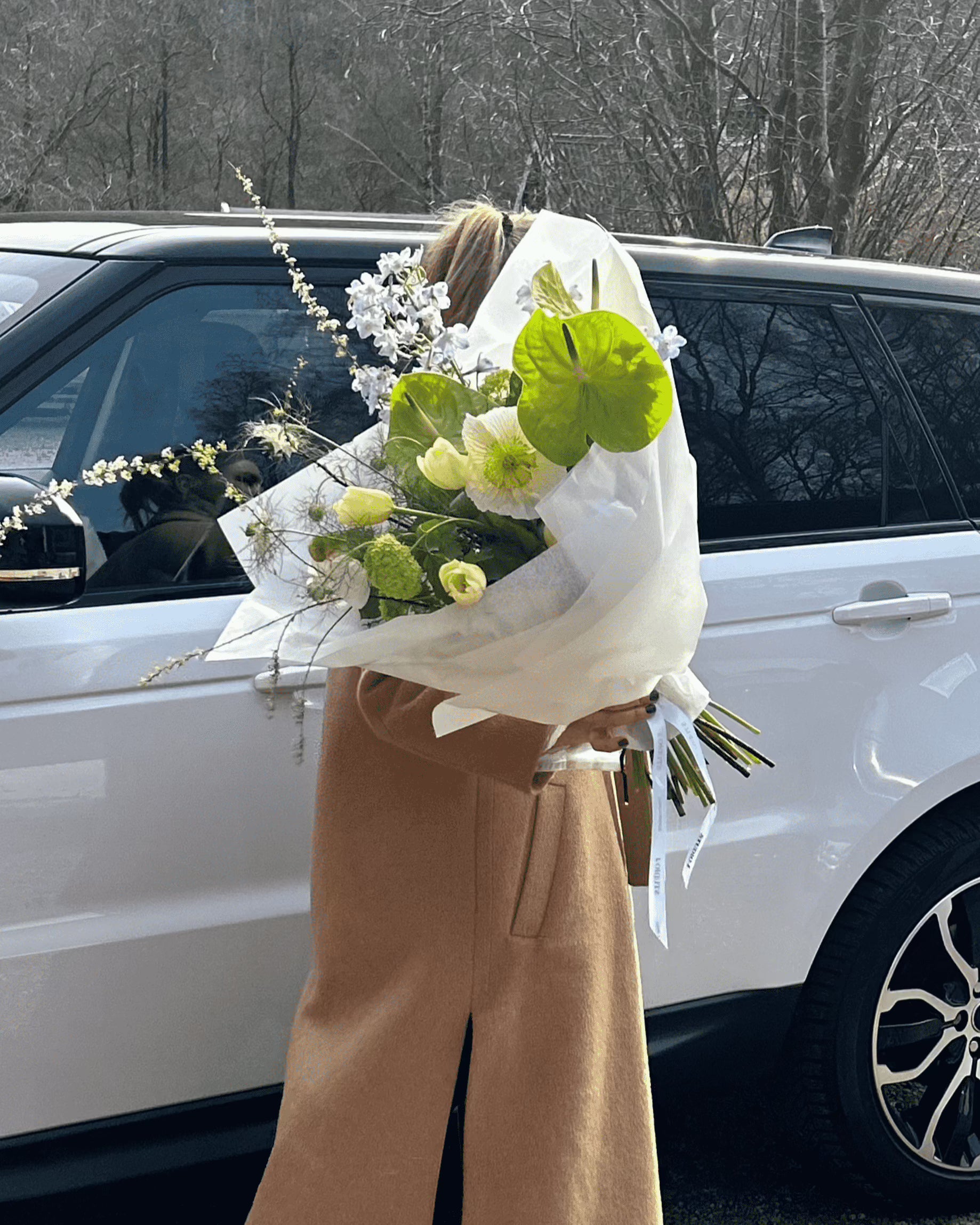 Kvinna som bär en vacker blombukett framför en vit bil