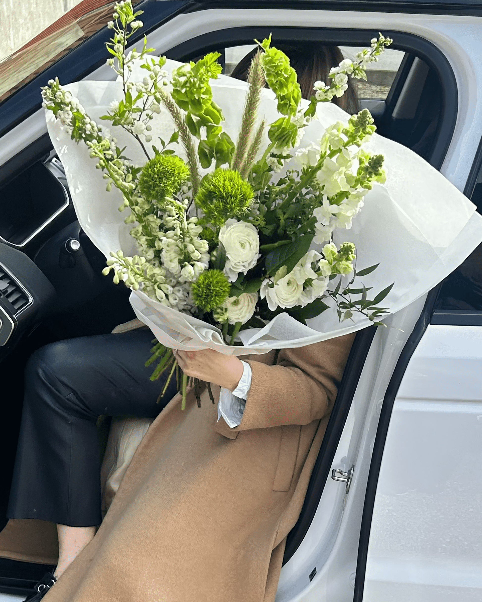 Kvinna som bär en vacker blombukett framför en vit bil