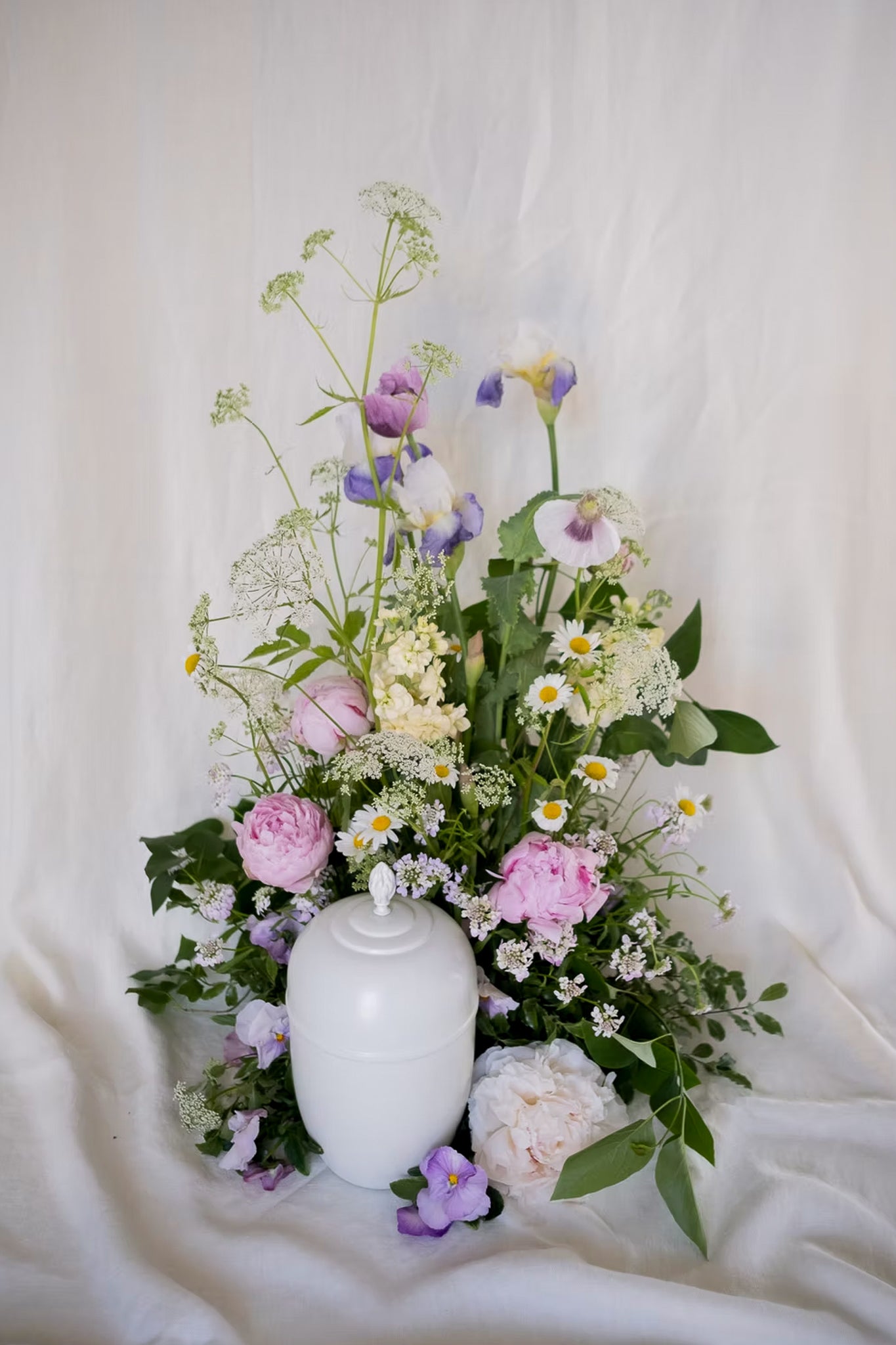 Begravningsdekoration med urna och blommor i lila och vitt